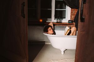 Photo of a shirtless man holding a book in a bathtub